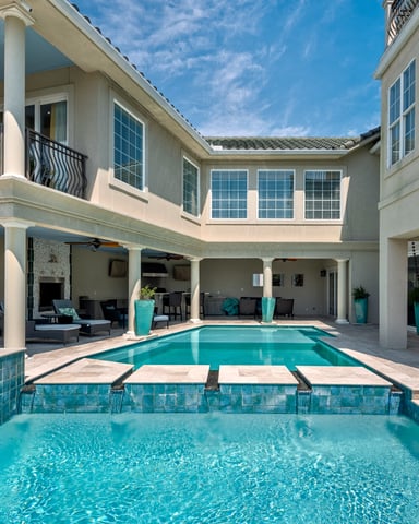 Luxury home with two swimming pools, covered patio with lounge chairs, and multi-story cream-colored facade with large windows